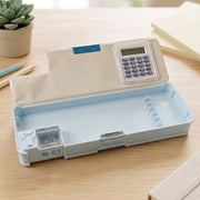 An open light blue pencil box with a calculator and sharpener, on a wooden desk with a succulent plant nearby.