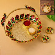 A golden kumkum dish with a peacock handle, holding red kumkum and white rice, with two matching lidded containers beside it.
