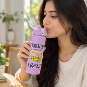 A person drinking from a medium-sized purple water bottle with a teddy bear design on a wooden table.