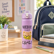 A medium-sized purple water bottle with a teddy bear design on a desk with school supplies and a backpack in the background.