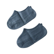 Two dark grey silicone shoe covers with textured soles are arranged on a plain white background.