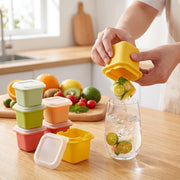 A person dispenses a citrus-infused ice cube from a yellow mold into a glass of water on a wooden counter, – view 3