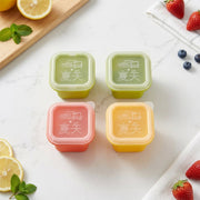 Four square silicone molds in green, pink, and yellow with clear lids, arranged on a white marble surface with lemons,