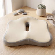A beige and grey ergonomic seat cushion on a wooden table with decorative rocks and a small plant.