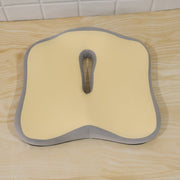 A beige and grey ergonomic seat cushion resting on a light wooden surface.