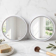 Two round white-framed mirrors on a white marble counter with soap and a makeup brush.