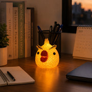 A yellow chick-shaped crystal texture LED lamp glowing on a light wooden desk with books and a calendar.