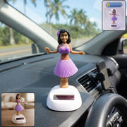 A solar-powered dancing hula girl toy in purple and brown, with a white base, on a car dashboard with an inset of its