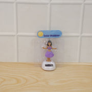 A solar-powered dancing hula girl toy in purple and brown, with a white base, in its clear plastic packaging.