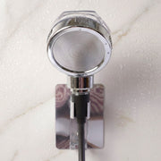 The chrome shower spray head is mounted on a wall bracket, with water droplets visible on the white marble surface.