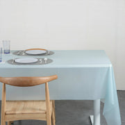 A light blue plastic table cover on a dining table set with two white plates and two glasses.