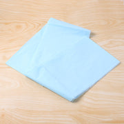 A light blue plastic table cover is unfolded and laid flat on a light brown wooden surface.