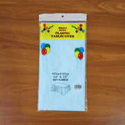 A light blue plastic table cover in clear retail packaging with text and balloon graphics on a wooden surface.