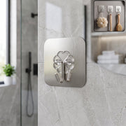 A single clover-shaped self-adhesive hook on a grey marble bathroom wall with a small plant in the background.