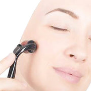 A woman with closed eyes gently rolls a black derma roller across her cheek.