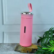 A pink vacuum flask with a silver lid and strap sits on a rock with green leaves and a white wall in the background.