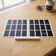 Two sheets of blank chalkboard labels and a white marker on a wooden table, with a small jar labeled 
