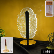 A glowing feather-shaped crystal table lamp with a gold base, a small inset, and a product code on a dark surface.