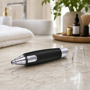 A black and silver nose hair trimmer lies on a marble counter with its clear cap next to it.