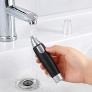 A hand holds a black and silver nose hair trimmer under running water in a white sink.