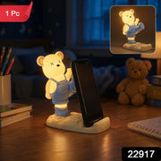 A glowing yellow bear phone holder with blue overalls on a desk at night, with a 