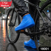 A person on a bicycle wears blue waterproof shoe covers on a wet city street, with a red 
