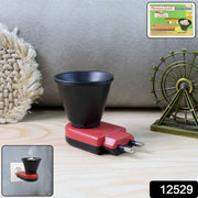 A red and black electric Kapoor Dani diffuser on a wooden surface with a decorative Ferris wheel and box.