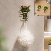 A green cartoon wolf hook holds a white bath pouf on a tiled bathroom wall, with an inset of two wolf hooks on a desk.