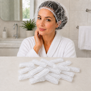 A woman in a white robe wearing a clear shower cap, with many folded shower caps on a counter below.