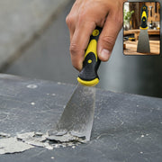 A hand uses a black and yellow handled putty knife to scrape paint chips from a dark surface.