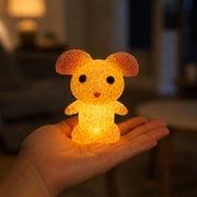 A yellow mouse-shaped crystal texture LED lamp glowing in the palm of a hand in a dimly lit room.