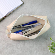 Open beige pencil case filled with pens, an eraser, and a stapler, next to a notebook.